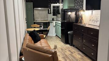 A cozy living room with a leather sofa, a dining table, and a kitchen area with a refrigerator and a television.