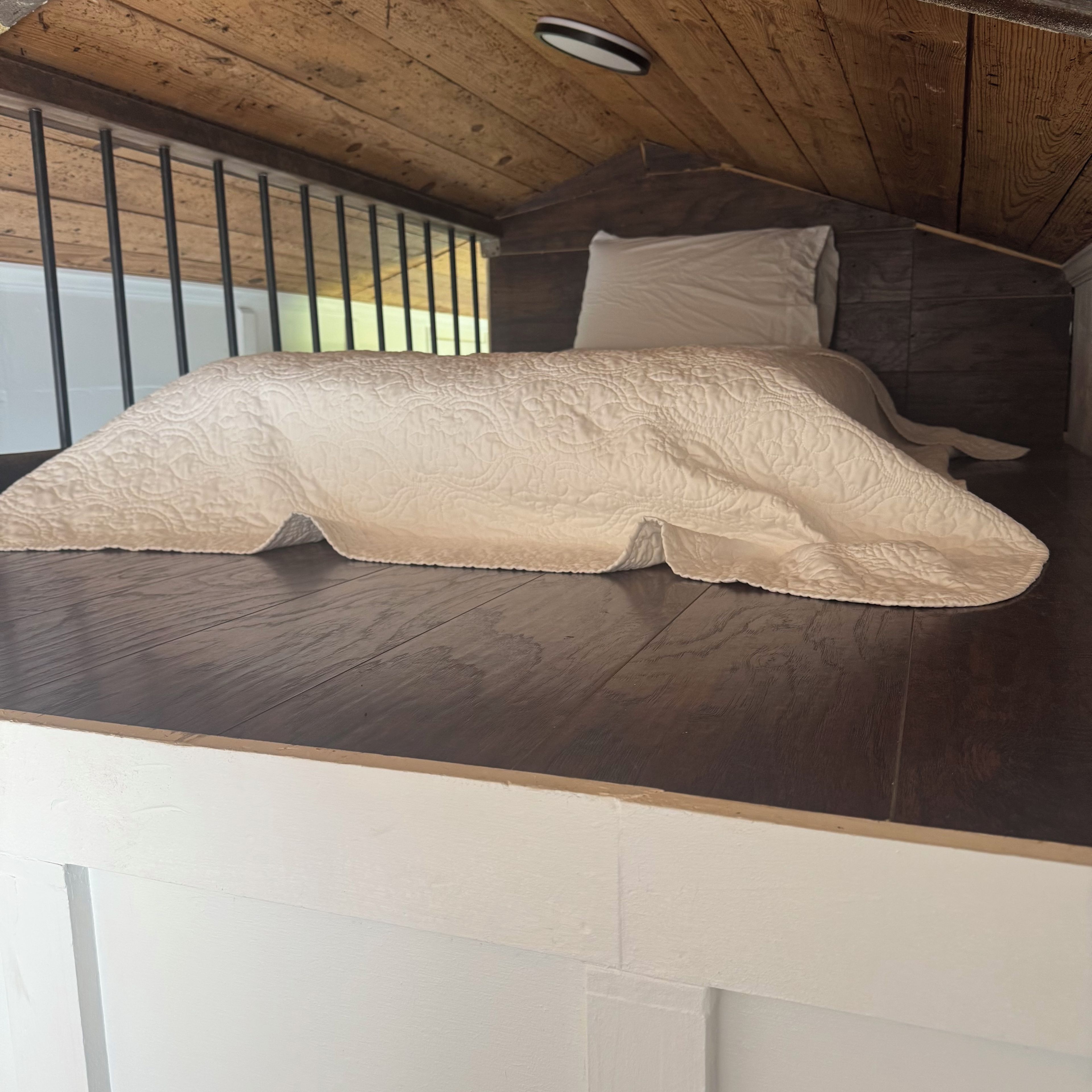 Una cama con cabecera acolchada, techo de madera y una ventana con rejas.