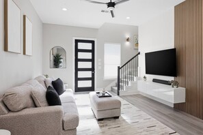 A modern living room with a sofa, a television, and a staircase leading to another room. - Summer + Fall Rates - 4BR - Game Nights + Backyard Vibes - 5 Min Dtwn (Dallas)