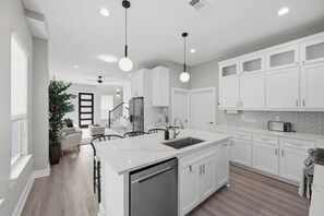A modern kitchen with white cabinetry, a central island with a sink, and pendant lighting. - Summer + Fall Rates - 4BR - Game Nights + Backyard Vibes - 5 Min Dtwn (Dallas)