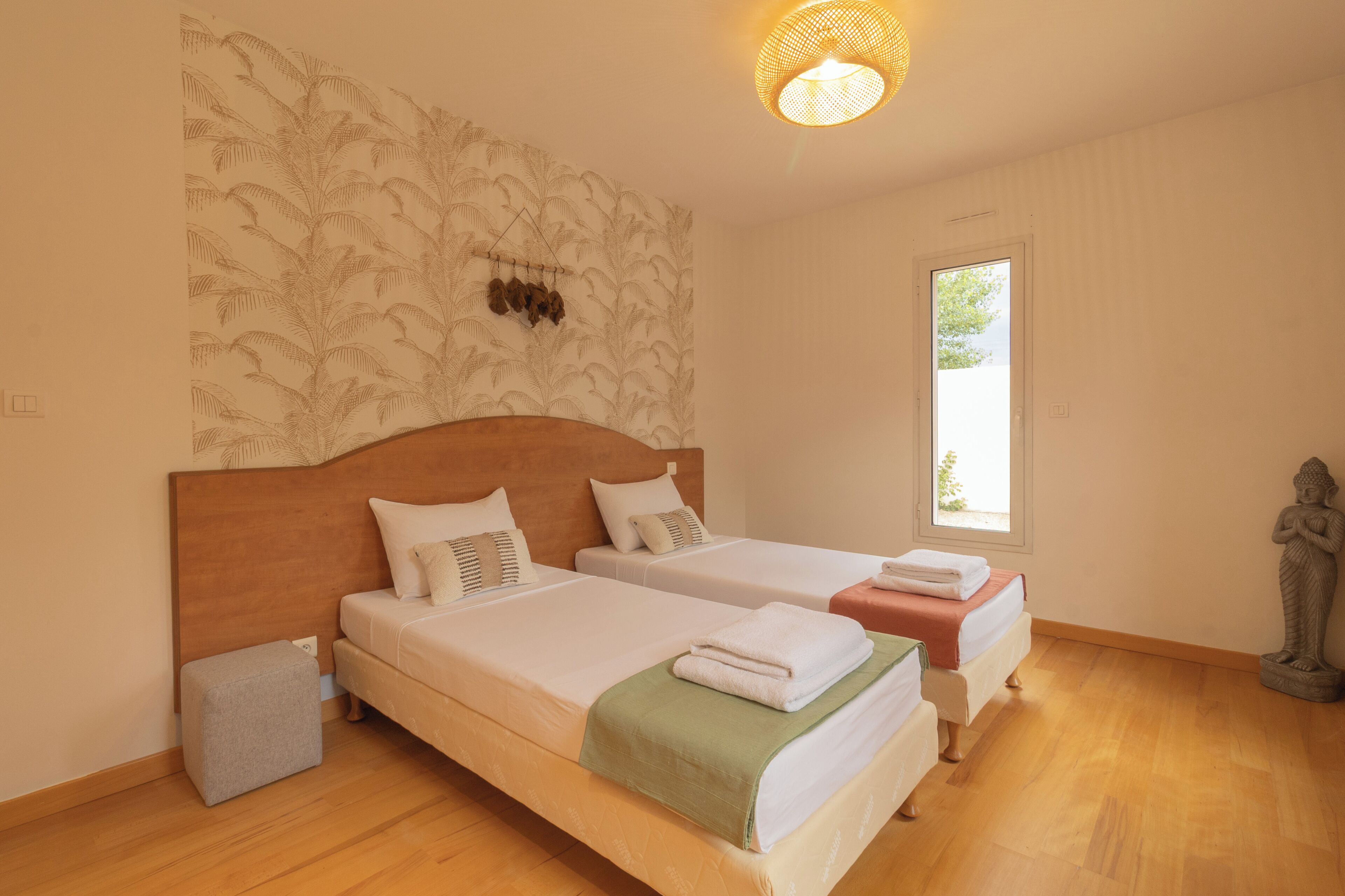 Een hotelkamer met twee bedden, een wandlamp, een raam en een beeldje.