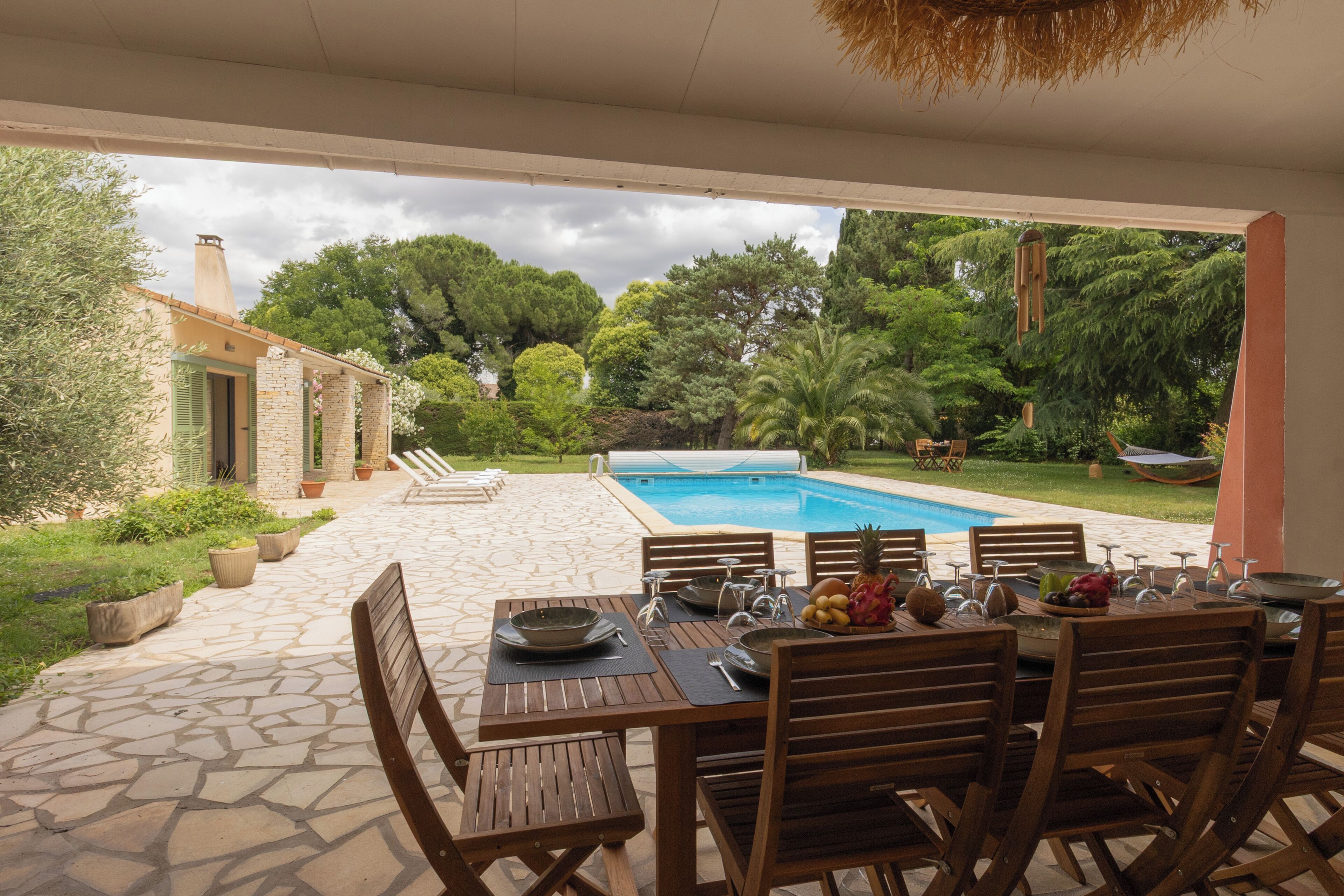 Zona pranzo all'aperto con piscina, pavimento in pietra e vegetazione lussureggiante.