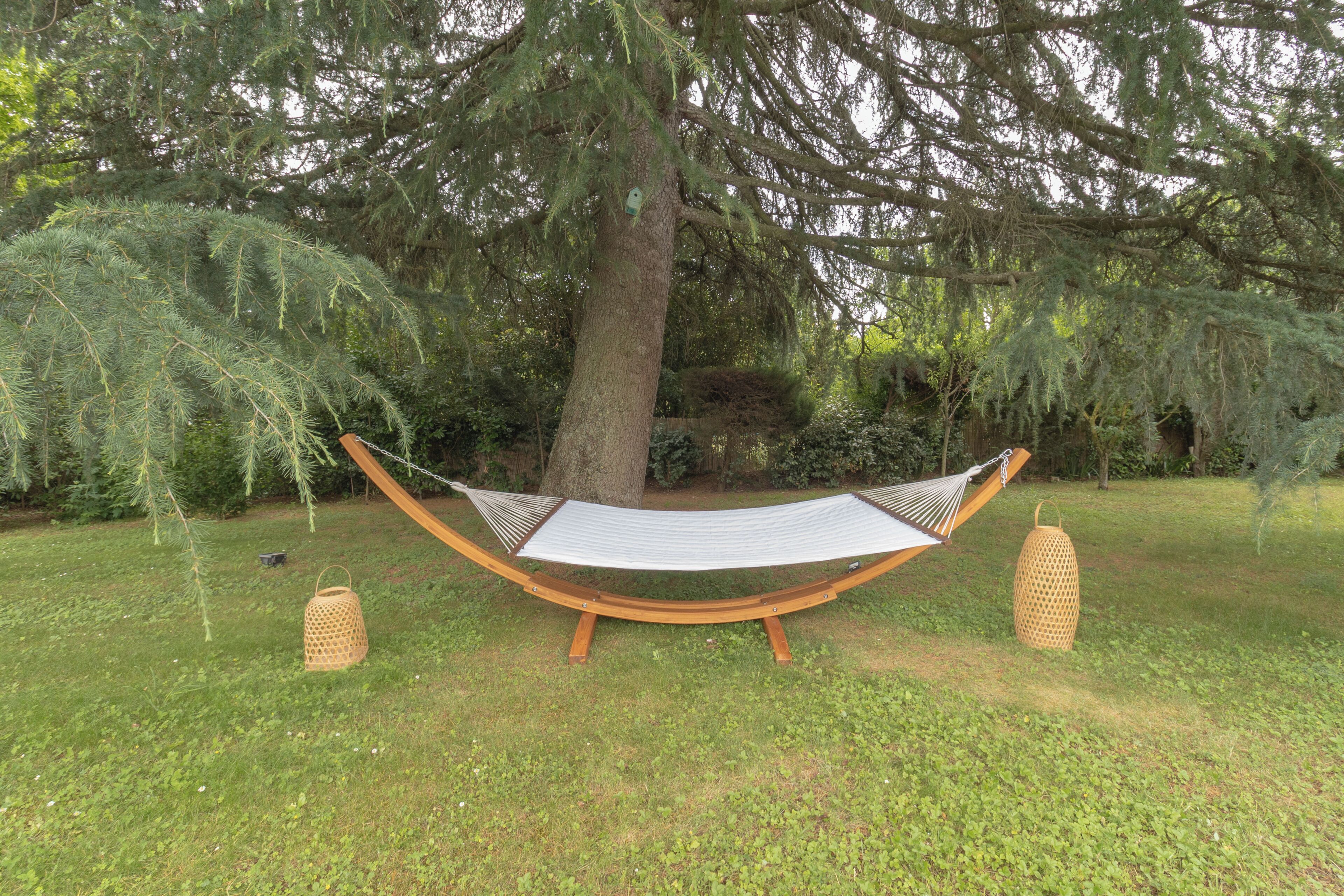 A hammock set up between two trees in a grassy area with a lantern on each side.