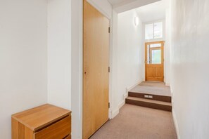 A hallway with a wooden door, a small wooden table, and a carpeted staircase leading to a room with a window. - Excellent 2 Bedroom Flat Next to Everything (Cambridge)