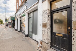A row of shops including Domino's, with a tiled mosaic wall and a black door with a keypad lock. - Excellent 2 Bedroom Flat Next to Everything (Cambridge)