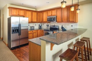 A kitchen with wooden cabinets, stainless steel appliances, granite countertops, and bar stools.