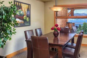 A dining area with a wooden table, leather chairs, a vase with red flowers, a painting on the wall, and a view of the outdoors through a window.