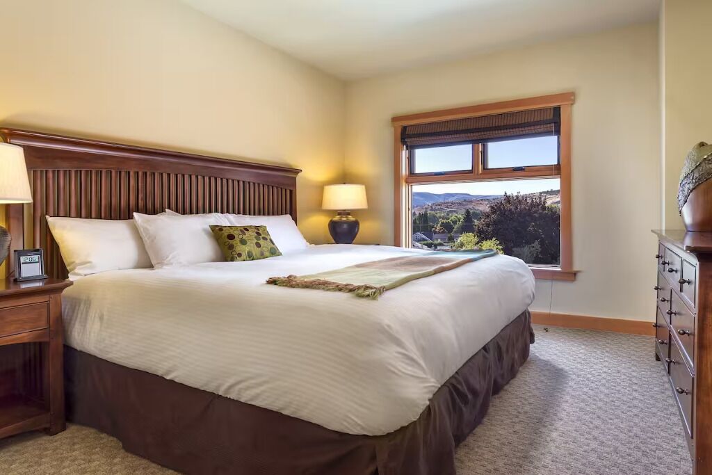 A hotel room with a large bed, a nightstand, a dresser, and a window with a view.