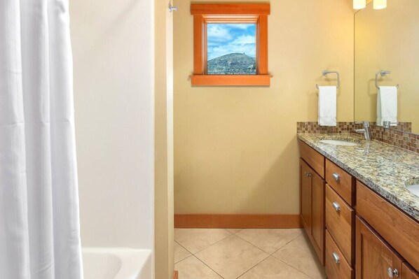 A bathroom with a window, a bathtub, a sink, and wooden cabinets.