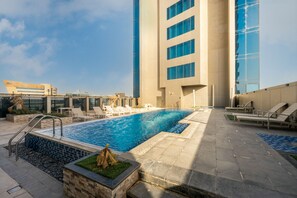 A rooftop pool area with lounge chairs and a view of a modern building. - Spacious 2-Bedroom aprt in Al Olaya (Riyadh)