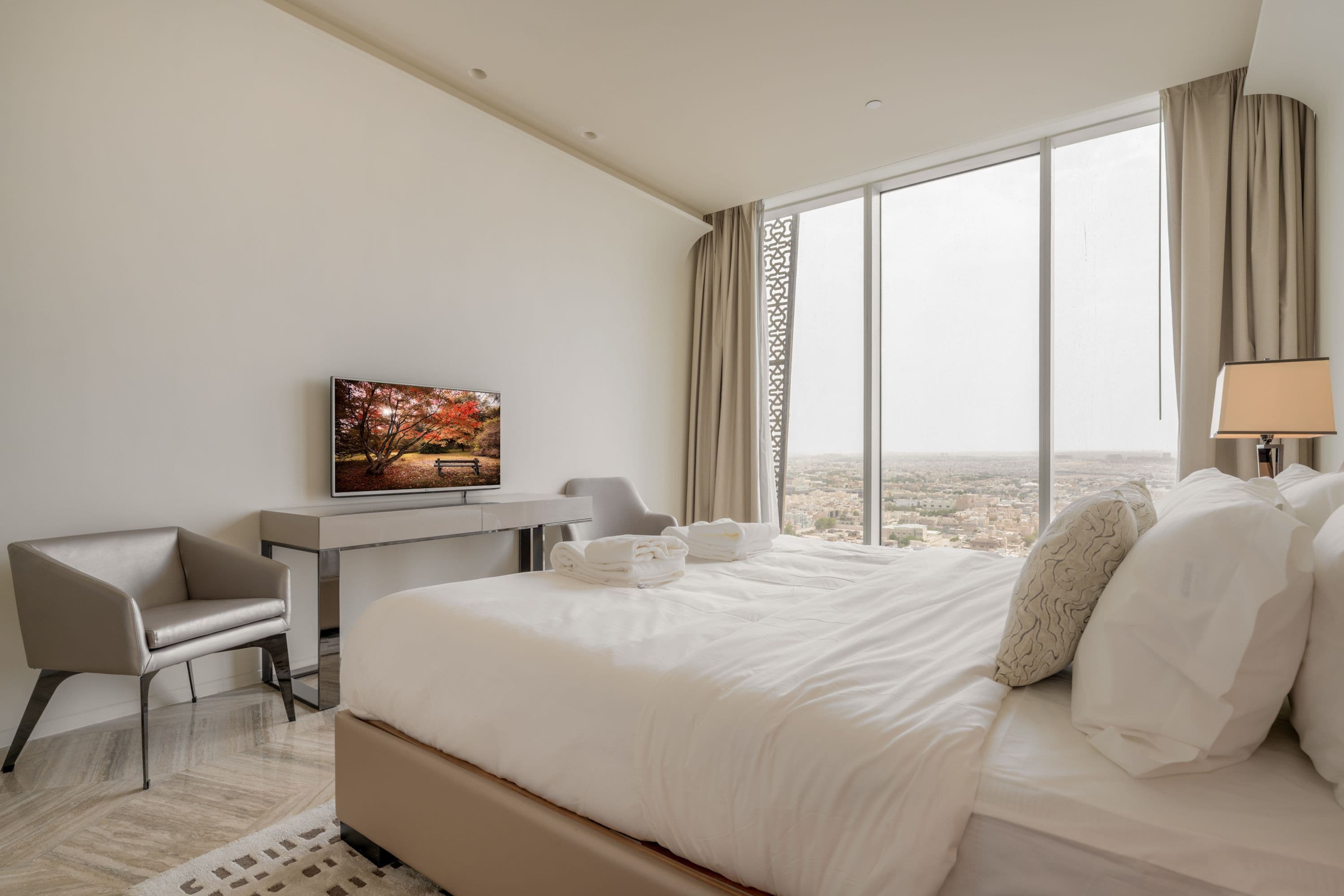 Quarto de hotel com uma cama grande, escrivaninha, cadeira, televisão e vista para a cidade.