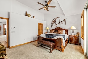 A bedroom with a large bed, a wooden bench, a ceiling fan, and wall-mounted decor. - Private Hot Tub, Pool, Ski Shuttle, Garage, Boot Warmer, Grill, Shuffle Board (Steamboat Springs)
