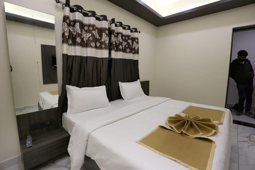A hotel room with a bed, a mirror, curtains, and a door.