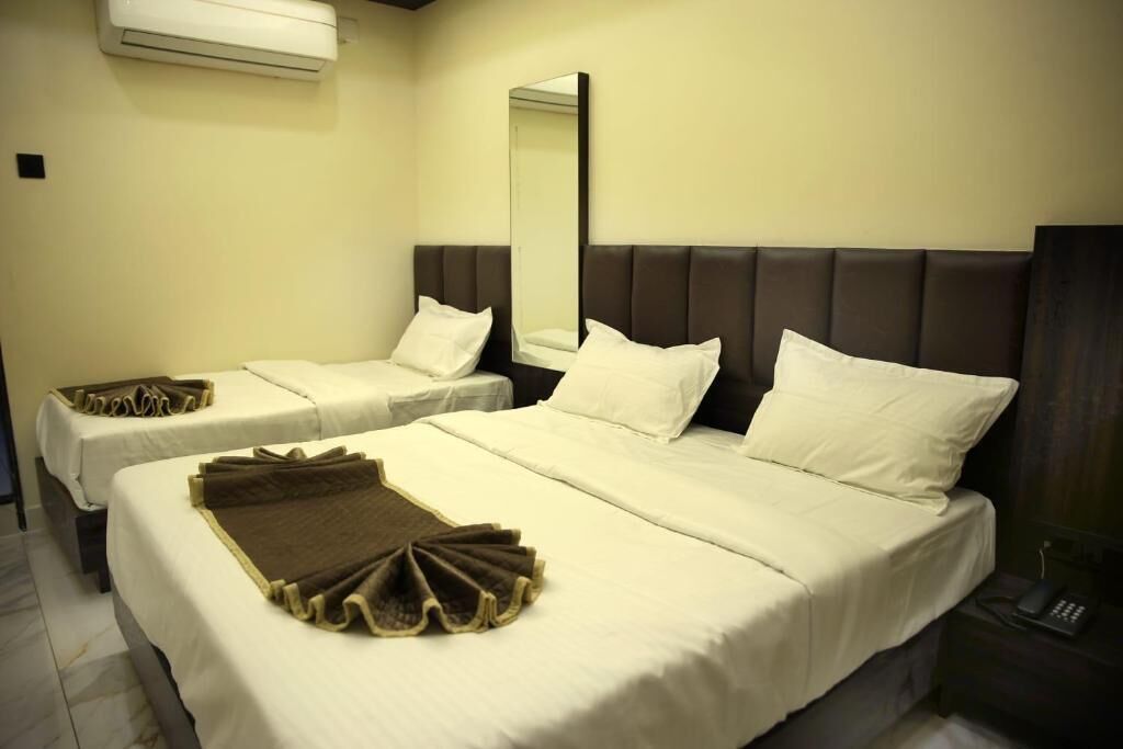 A hotel room with two beds, a large mirror, and a bedside telephone.