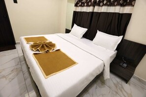 A hotel room with a bed, a bedside table with a phone, and a curtain with a floral pattern. - Hotel Bansi palace (Dwarka)