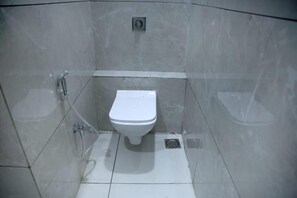 A small, enclosed bathroom with a toilet, a shower, and a sink. - Hotel Bansi palace (Dwarka)