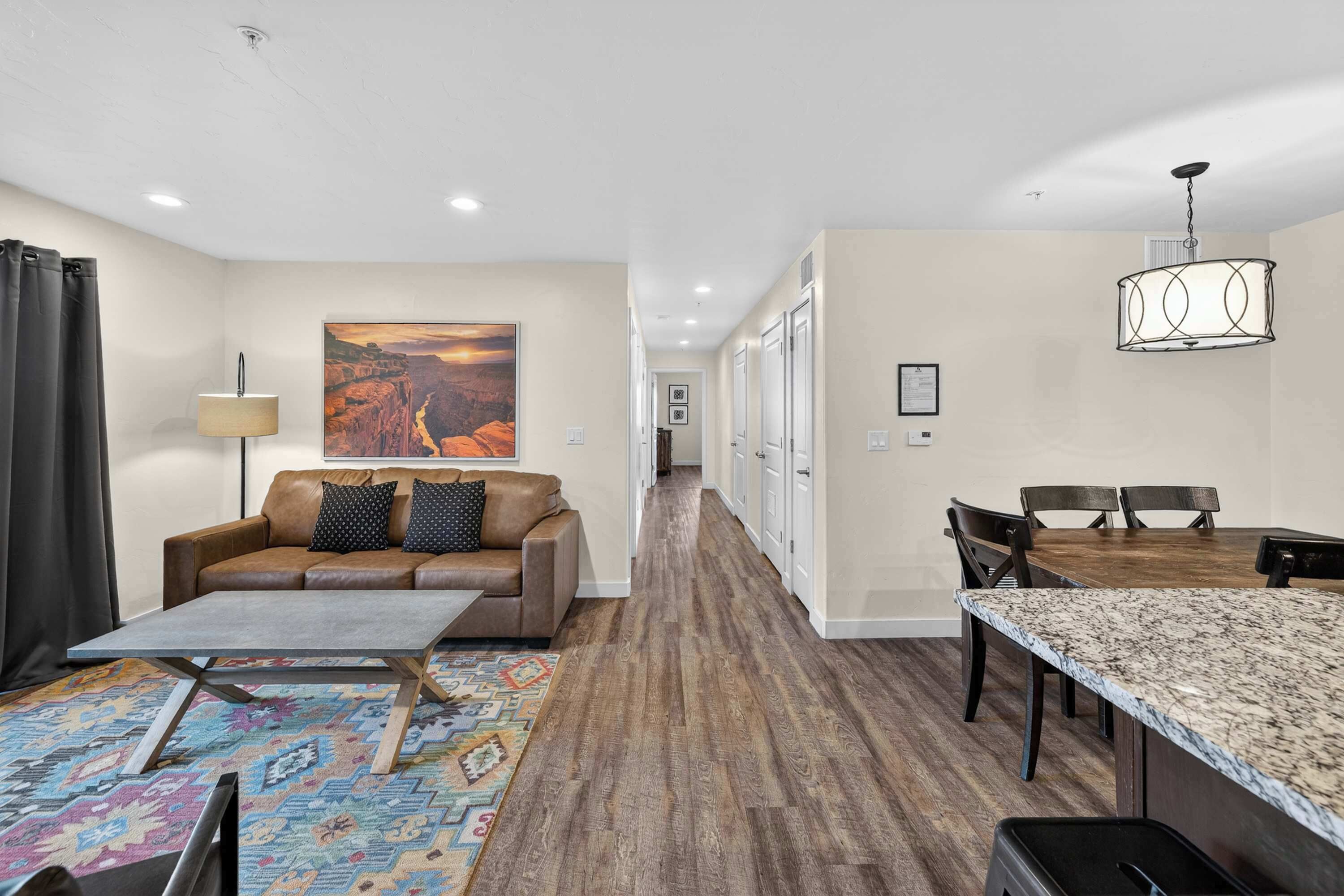Une chambre d’hôtel moderne, dotée d’un canapé, d’une table basse, d’un tapis à motifs, d’une table à manger, de chaises et d’un tableau accroché au mur.