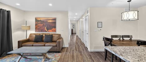 Une chambre d’hôtel moderne, dotée d’un canapé, d’une table basse, d’un tapis à motifs, d’une table à manger, de chaises et d’un tableau accroché au mur.