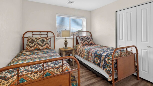 A bedroom with two wooden beds, a nightstand, a lamp, and a window with blinds. - 2-B Grand County Redcliff Condo (Moab)