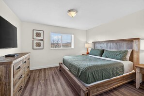 A bedroom with a bed, a dresser, a TV, and a window with blinds. - 2-B Grand County Redcliff Condo (Moab)