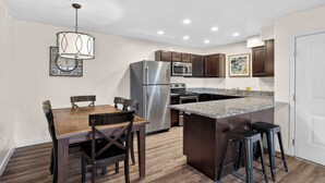 A modern kitchen with a stainless steel refrigerator, microwave, and stove, wooden dining table, and bar stools. - 2-B Grand County Redcliff Condo (Moab)