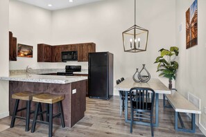 A modern kitchen with wooden cabinets, a black refrigerator, a granite countertop, and a dining area with a table and chairs. - 4-I White Rim Redcliff Condo (Top Floor) (Moab)