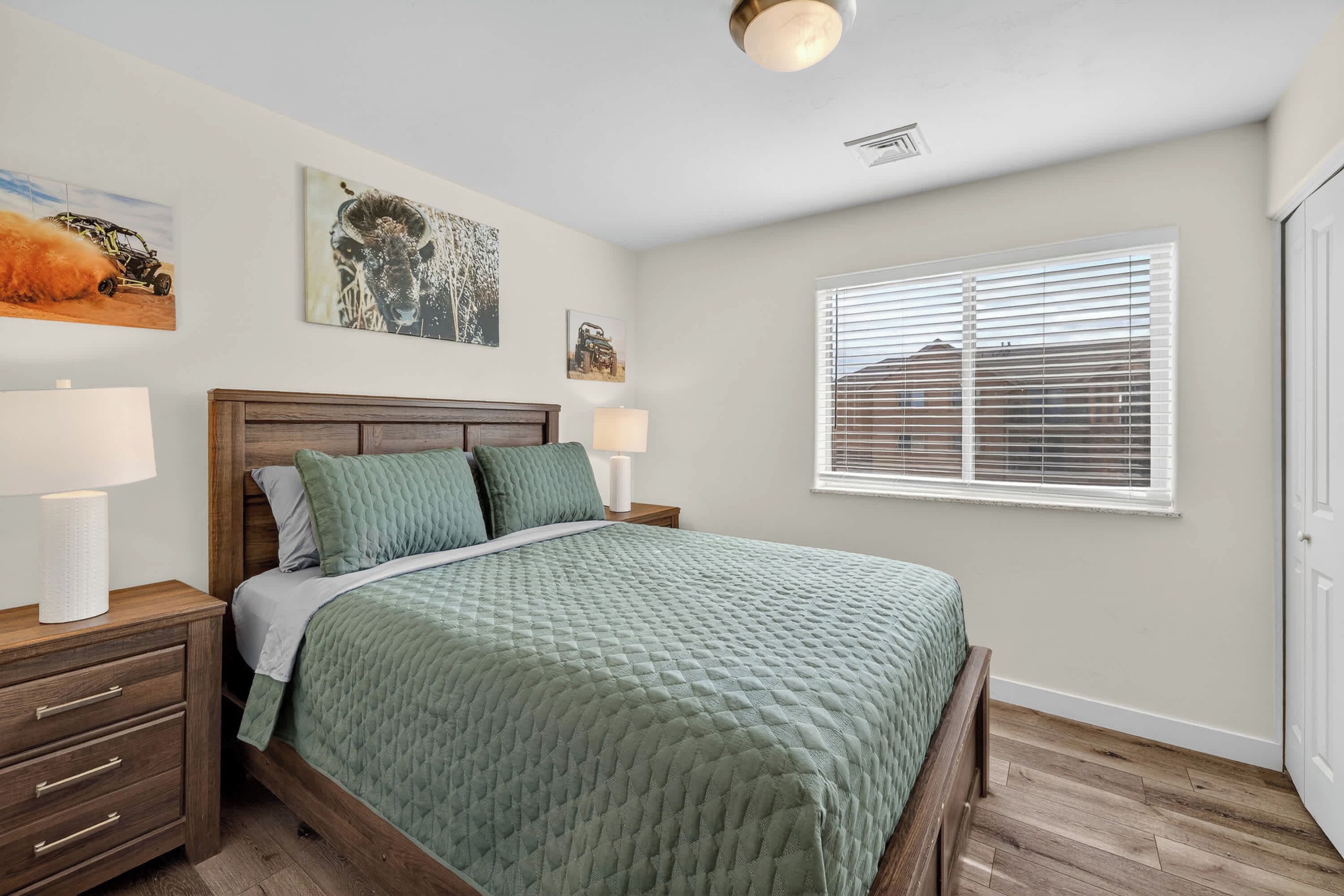 A bedroom with a bed, nightstands, a window with blinds, and wall art.
