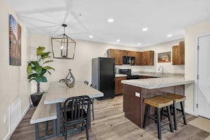 A modern kitchen with wooden cabinets, a central island with stools, a refrigerator, and a microwave. - 4-A Arches Redcliff Condo (Ground Floor) (Moab)