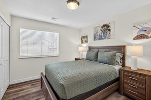 A bedroom with a bed, two bedside tables with lamps, a window with blinds, and wall art. - 4-A Arches Redcliff Condo (Ground Floor) (Moab)
