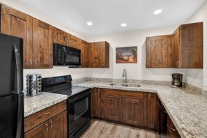 A kitchen with wooden cabinets, a black refrigerator, a microwave, a stove, and a granite countertop. - 4-A Arches Redcliff Condo (Ground Floor) (Moab)