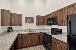 Eine Küche mit Holzschränken, einer Edelstahlspüle, einem schwarzen Kühlschrank und einer Mikrowelle.