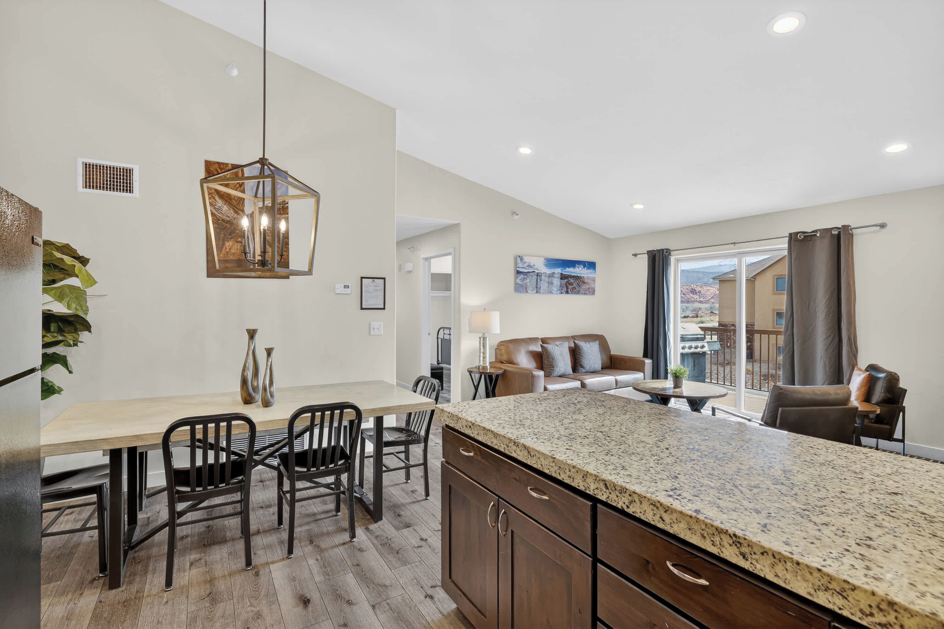 A modern kitchen with a granite countertop, wooden cabinets, and a dining area with chairs and a table.