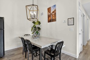 Ein Essbereich mit einem Holztisch, schwarzen Stühlen, einer hängenden Leuchte, einem Topfpflanzen und gerahmten Kunstwerken an der Wand.