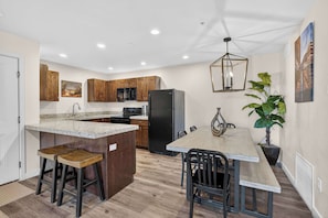 A kitchen with wooden cabinets, a granite countertop, a black refrigerator, and a dining area with a table and chairs. - 4-B Slick Rock Redcliff Condo (Pool View) (Moab)