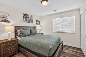 A bedroom with a bed, two bedside tables with lamps, a window with blinds, and wall art. - 4-B Slick Rock Redcliff Condo (Pool View) (Moab)