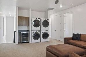 A laundry room with four stacked front-loading washing machines, a built-in dryer, and a small cabinet. - Moab Desert Oasis Pool Spa Red Rock Views (Moab)