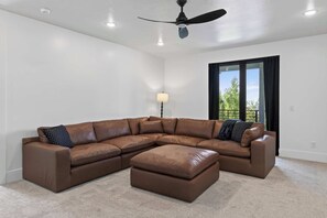 Ein geräumiges Wohnzimmer mit einem großen, in L-Form angeordneten Schlafsofa, einem Deckenventilator und Blick durch ein großes Fenster.