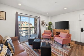 A living room with a sofa, two armchairs, a television, and a balcony with a table and chairs. - 2-E Copper Ridge Condo (Moab)