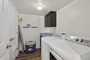 Ein Waschraum mit einer Frontlader-Waschmaschine und einem Trockner, einer blauen Aufbewahrungsbox, einer Leiter und einem schwarzen Schrank.