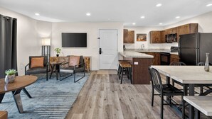 A modern kitchen with wooden cabinets, a black refrigerator, and a dining area with a table and chairs. - 4-D Colorado River Redcliff Condo (Ground Floor) (Moab)