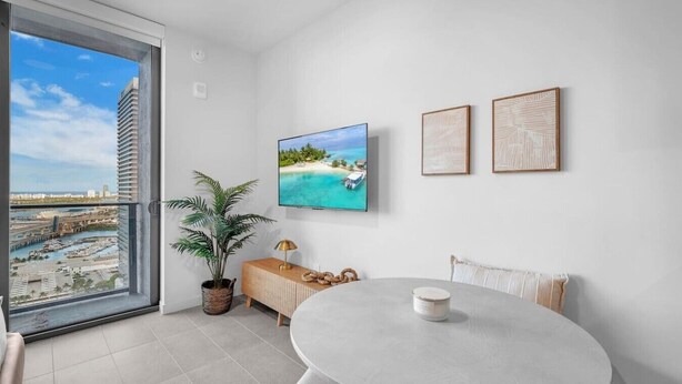 A modern room with a large window, a flat-screen TV, a dining table, and a potted plant. - Urban Escape Suite | Ocean View | Downtown (Miami)