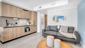 A modern kitchen with wooden cabinets and a built-in oven, a grey sofa with cushions, and a round rug with two stools. - Urban Escape Suite | Ocean View | Downtown (Miami)