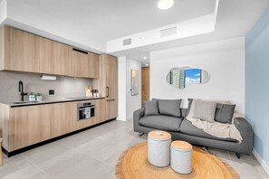 Eine moderne Küche mit Holzausstattung und einem eingebauten Ofen, ein graues Sofa mit Kissen und ein runder Teppich mit zwei Hocker.