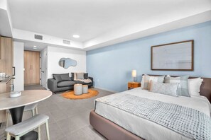 A modern hotel room with a bed, bedside table, and a seating area with a sofa and ottoman. - Urban Escape Suite | Ocean View | Downtown (Miami)