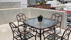 A rooftop terrace with a table and chairs, a potted plant, and a view of a cityscape including a tall building under construction. - Lovely 1-bedroom Rental Unit in Mazatlán Centro (Mazatlán)