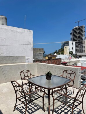 A rooftop terrace with a table and chairs, a potted plant, and a view of a cityscape including a tall building under construction. - Lovely 1-bedroom Rental Unit in Mazatlán Centro (Mazatlán)