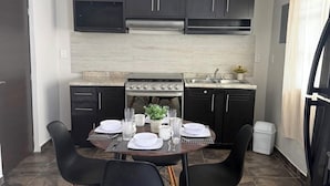 A compact kitchen with dark cabinets, a stove, and a dining table set for four. - Lovely 1-bedroom Rental Unit in Mazatlán Centro (Mazatlán)