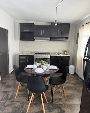 A compact kitchen with dark cabinets, a stove, and a dining table set for four. - Lovely 1-bedroom Rental Unit in Mazatlán Centro (Mazatlán)