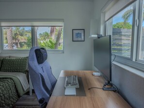 A room with a desk, a computer, a chair, a bed with a green blanket, and a window with a view of palm trees and a fence. - 3BR 2BA house, Jacuzzi, Minutes to beach, in fabulous Fort Lauderdale with AC (Fort Lauderdale)