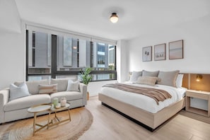 A modern bedroom with a large bed, a sofa, a small table, and a nightstand. - Brand New Building & Amazing Amenities (Miami)